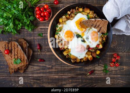 Spiegeleier mit Gemüse - shakshuka in der Pfanne und Roggenbrot auf einem alten hölzernen Hintergrund. Spätes Frühstück. Rustikaler Stil. Mittelöstlicher Tradit Stockfoto