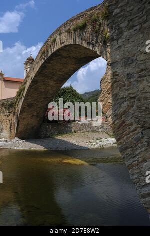 Der 33. Jahrhundert einbögiger Ponte Vecchio oder Alte Brücke in Dolceacqua, Imperia, Ligurien, Italien hat einen anmutigen, 108 m langen ‘d, einböggen „monkey back“, der den Fluss Nervia überspannt. Sie wurde im Februar 1884 vom französischen Impressionismus-Gründer Claude Monet als „un bijou de légèreté“ (ein Juwel der Leichtigkeit) beschrieben. Zwei Tage später malte er sowohl die Brücke als auch das zerstörte Doria-Schloss aus dem 16. Jahrhundert, das sich am unteren Hang des Monte Rebuffo befindet und Terra, die Altstadt von Dolceaqua, dominiert. Stockfoto