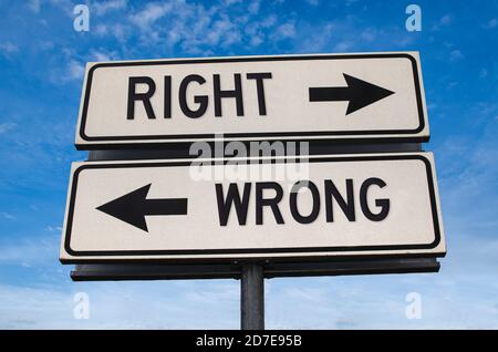Richtig oder falsch. Weiße zwei Straßenschilder mit Pfeil auf Metallmast mit Wort. Richtungsstraße. Kreuzung Straßenschild, Zwei Pfeil. Blauer Himmel Hintergrund. Stockfoto