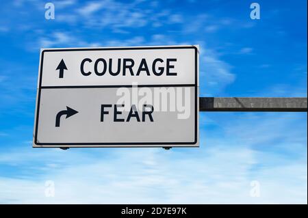 Mut versus Angst. Weiße zwei Straßenschilder mit Pfeil auf Metallmast. Richtungsstraße. Kreuzung Straßenschild, Zwei Pfeil. Blauer Himmel Hintergrund.