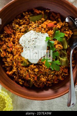 Reis mit Gemüse und Joghurt. In Steingut auf einem Leinentischtuch Stockfoto
