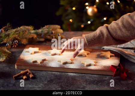 Womans Hand Greift Nach Frisch Gebackenen Sternförmigen Weihnachtsplätzchen An Bord Mit Puderzucker Bestäubt Stockfoto