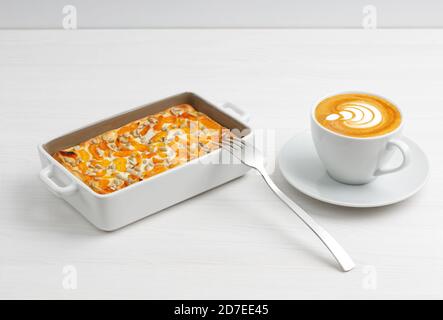 Tasse Kaffee und hausgemachter Hüttenkäse-Auflauf mit getrockneten Aprikosen und Sonnenblumenkernen auf weißem Holztisch. Stockfoto