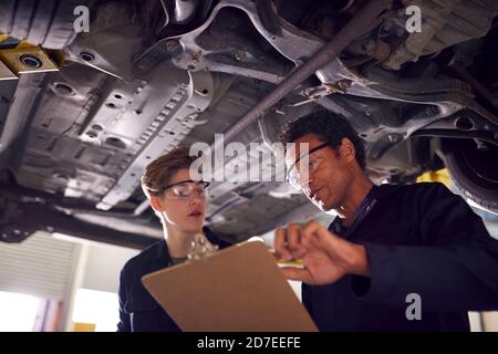 Männlicher Tutor Mit Student Blick Unter Auto Auf Hydraulische Rampe Auf Auto Mechanic Course Stockfoto