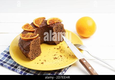 Gelbe Platte mit einem halben hausgemachten Schokoladenkuchen mit dekoriert Kandierte Orangenscheiben auf weißem Holztisch Stockfoto