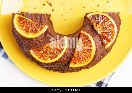 Nahaufnahme ein halber hausgemachter Schokoladenkuchen mit kandierten Orangenscheiben auf gelbem Teller dekoriert. Draufsicht. Stockfoto