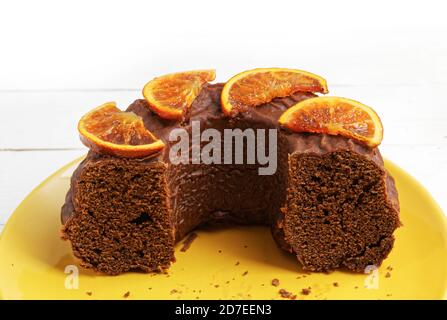 Nahaufnahme ein halber hausgemachter Schokoladenkuchen mit kandierten Orangen dekoriert Scheiben auf gelber Platte Stockfoto