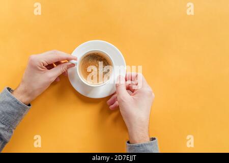 Die Hände des Mannes halten eine Tasse Kaffee auf dem gelben Tisch Stockfoto