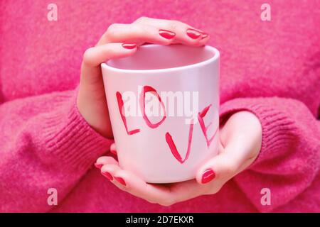 Weibliche Hände halten eine rosa Tasse mit der Aufschrift Liebe Stockfoto