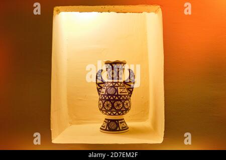 Arabische Tonvase blau mit weißen Mustern. In einer Nische in der Wand steht eine Amphore mit abstraktem Muster. Vase im arabischen Stil, auf einem Sockel. Stockfoto