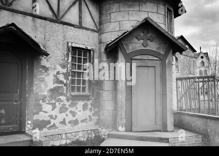 Schwarz-Weiß-Foto der alten Kirche. Geschlossene Tür mit einem Kreuz über dem Eingang, monochrom Stockfoto