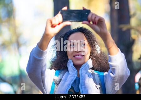 Nahaufnahme einer lächelnden afroamerikanischen Frau im Wald, die ein Selfie auf einem Smartphone gemacht hat. Sie schickt Fotos an ihre Freunde. Stockfoto