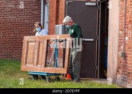 Frederick, MD, USA 10/14/2020: Ein Paar mit Gesichtsmaske wegen COVID-19 ersetzt eine Tür in ihrem Geschäft. Sie verluden die Tür auf einen Plattformwagen Stockfoto