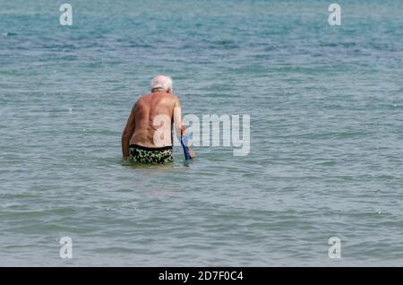 Der alte Herr am Meer läuft und tritt ins Wasser ein Mit dem Stick Stockfoto