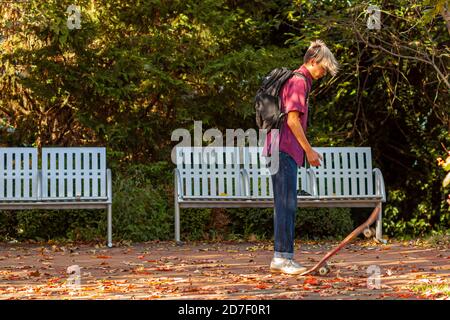 Frederick, MD, USA 10/14/2020: Ein Teenager-Junge mit stylischen blonden Haaren, die Jeans und Sneakers tragen, tritt auf den Schwanz seines Skateboards, um es in Th zu knallen Stockfoto