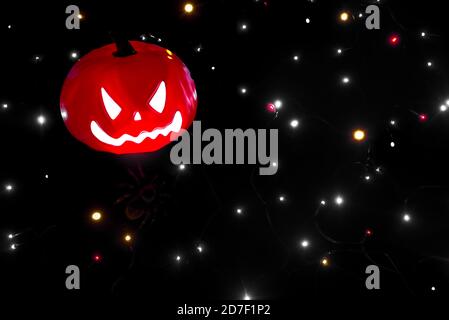 Gruselig dunkel orange Halloween Kürbis mit Spinne nahe Mund, Lichter auf schwarzem Hintergrund und mit Kopierraum. Plastikkürbis leuchtet im Dunkeln Stockfoto