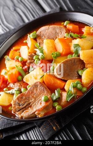 Kartoffeln schmoren Karotten Erbsen Rinderzunge und Tomaten in einer Schüssel auf dem Tisch. Vertikal Stockfoto