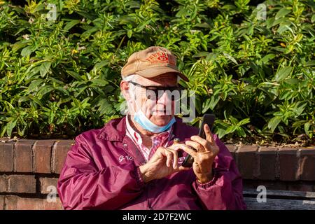 Frederick, MD, USA 10/14/2020: Ein älterer Kaukasusmann versucht, eine Nummer auf der Tastatur seines alten Flip-Telefons zu wählen, während er eine Zigarre dazwischen hält Stockfoto