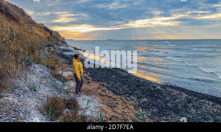 Sonnenaufgang über dem Meer. Schöne Landschaft mit langer Belichtung mit Frau am Meer und die Sonne scheint durch die Wolken. Vintage-Foto von Coblevo Ukraine Stockfoto