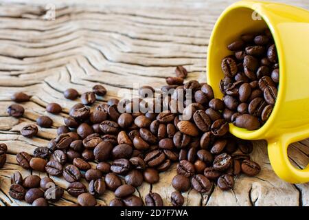 Kaffeebohnen und gelbe Tasse. Kaffeebohnen kommen aus einer kleinen gelben Tasse auf den Tisch Stockfoto