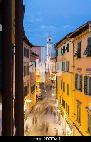 Fußgänger, die am Abend den Corso Italia mit dem Uhrturm im Hintergrund entlang gehen, Pisa, Toskana, Italien Stockfoto