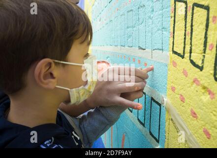 Der Künstler hilft dem Jungen, mit dem eigenen Finger an die Wand zu malen. Das Kind trägt Gesichtsmaske Stockfoto