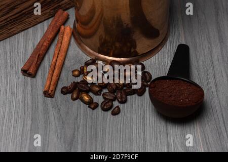 Verstreute Kaffeebohnen, Zimtstangen, gemahlener Kaffee im Löffel, Kaffeemühle auf grauer Holzoberfläche Stockfoto