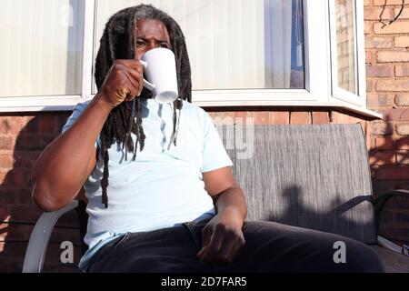 Der Mann saß im Garten und trank aus der Tasse, während er in Richtung schaute So Stockfoto