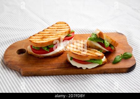 Leckere gegrillte Caprese Panini (Mozzarella, Tomaten und Basilikum) auf einem rustikalen Holzbrett, Seitenansicht. Stockfoto