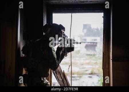 Soldat in voller US MARSOC bewaffnet mit Sturmgewehr durch das verlassene Gebäude laufen. Militärischer Zusammenstoß. Stockfoto