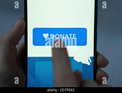 Nahaufnahme Finger Drücken spenden Symbol-Taste auf blauem Bildschirm auf schwarzem Handy. Spendengeld Online-Konzept. Stockfoto