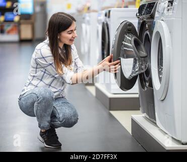 Eine junge Frau in einem Geschäft wählt eine Waschmaschine.. Das Konzept des Shoppings. Stockfoto