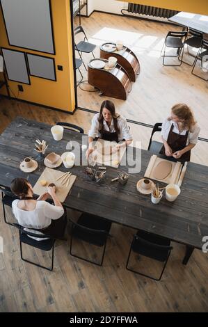 In der Tonwerkstatt. Töpferinnen sprechen und lächeln während des Arbeitsprozesses in der Tonwerkstatt. Weibliche Töpfer Meister Rollen den Ton auf Stockfoto