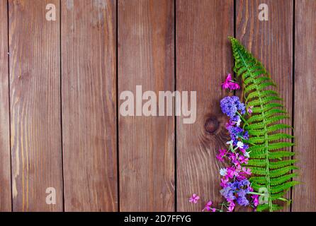 Farn und bunte Blumen liegen auf einem hölzernen Hintergrund Stockfoto