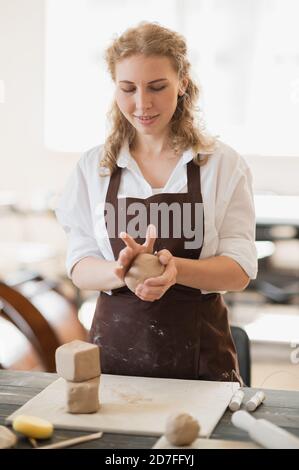 Die Meisterin knetet Ton neben einem Holztisch in einer Töpferwerkstatt Stockfoto