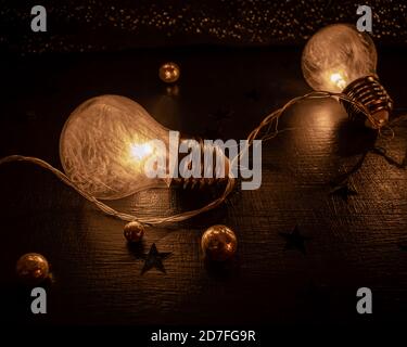 Nahaufnahme von zwei Glühbirnen mit winzigen weißen Federn Auf einer dunklen Oberfläche und mit Glitzerkugeln und verziert Sterne Stockfoto