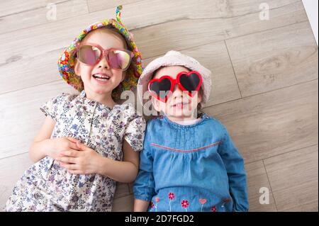 Kinder in lustigen Gläsern liegen auf dem Boden und lachen.wenig Mädchen liegen auf dem Rücken und lachen Stockfoto