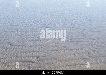Texturen von Wasser und Wind auf dem Sand am Strand, Reflexionen einer Windmühle und Licht im Wasser Stockfoto