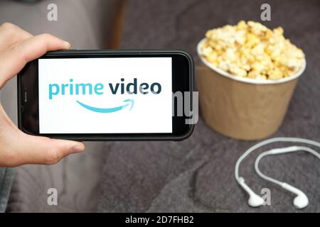 Nahaufnahme mans Hand hält ein Handy mit Prime Video Amazon-Logo mit Apple-Kopfhörer und Popcorn-Box neben ihm, August 2020, San Francisco Stockfoto