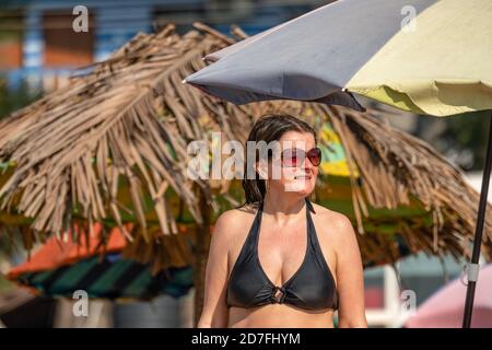 Hübsche skandinavische Frauen mittleren Alters in Sonnenbrillen mit feuchter Haut und Bikini nach dem Schwimmen im Meer, Blick zur Seite. Sonniger Tag, tropisch re Stockfoto