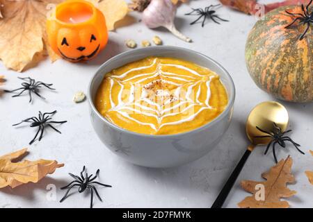 Halloween Kürbissuppe mit cremigem Spinnennetz in grauer Schale und Spinnen auf dem Tisch. Nahaufnahme Stockfoto