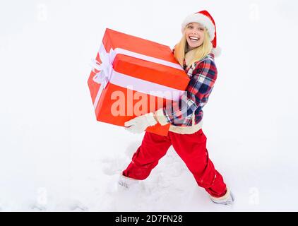 Frau trägt ein großes Geschenk isoliert auf Schnee Winter Hintergrund - voller Länge. Lustige Frau hält ein großes Weihnachtsgeschenk. Stockfoto