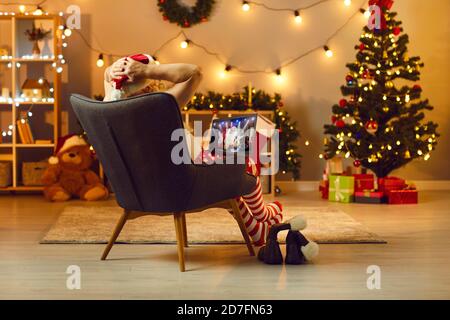 Entspannter reifer Mann sitzt in einem Sessel zu Hause beobachten Video mit Santa Claus DJ auf Laptop Stockfoto