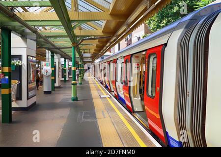 Der Bahnsteig der Londoner U-Bahn ist fast leer, eine Person in der Ferne besteigen den Zug mit allen geöffneten Türen. Die Station befindet sich auf einem Open-ai Stockfoto