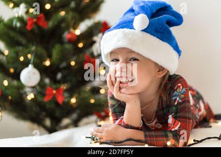 frohe Weihnachten und glückliches neues Jahr, Kindheit, Urlaub Konzept - close-up kleines lächelndes Mädchen in blauen weihnachtsmann Hut auf seinem Bauch spielen und Spaß haben Stockfoto