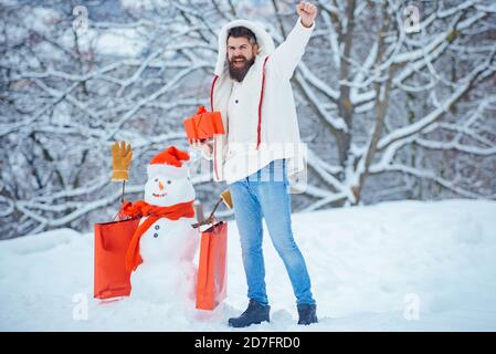 Weihnachtseinkäufe mit Einkaufstasche. Mann mit rotem Geschenk spielt mit Schneemann im Winter Park. Weihnachtsbanner. Glücklicher Vater mit Weihnachtsgeschenk vorbei Stockfoto