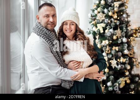 Gemeinsam Weihnachten feiern. Junges Paar in Ferienkleidung umarmt in der Nähe des Weihnachtsbaums. Neujahr, Valentinstag, Liebe, Romantik Konzept. Stockfoto