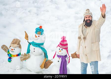 Schneemann und lustiger bärtiger Mann im Schnee. Wintermann. Weihnachten Winter Menschen. Winter Porträt von jungen schönen Hipster im Schnee Garten machen Schneemann. Stockfoto