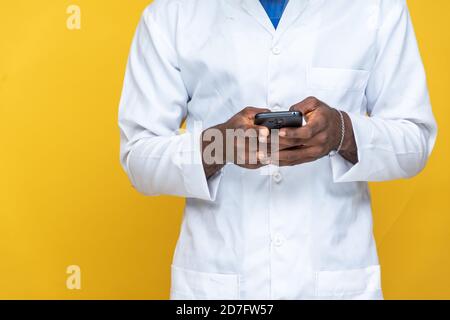 Nahaufnahme eines jungen schwarzen Mannes in einem Labormantel Über sein Telefon Stockfoto
