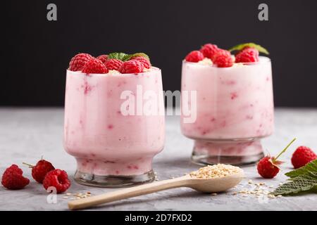 Joghurt mit Himbeere und Sesam in Glas und Holzlöffel auf grauem und schwarzem Hintergrund. Seitenansicht, Nahaufnahme. Stockfoto